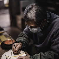 真剣な眼差しで陶器に絵付けをする直方市の陶芸家の写真