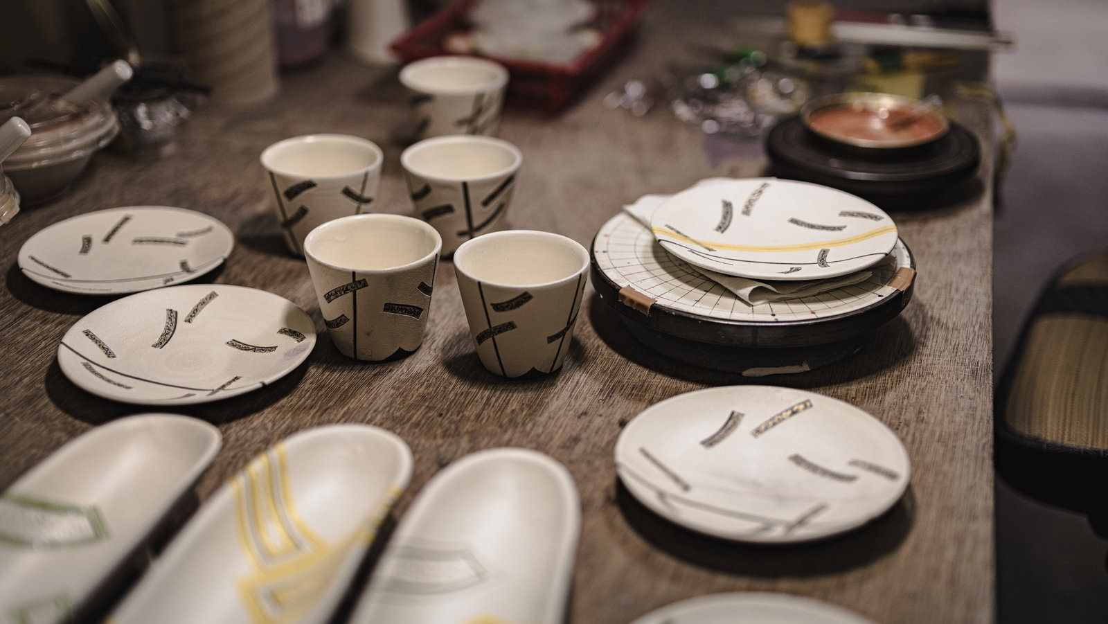 陶芸工房の作業台に並ぶ制作中の白い湯呑みや皿などの陶器作品
