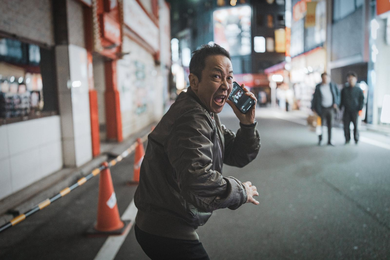 Man running and looking back while holding a smartphone in a busy nighttime district