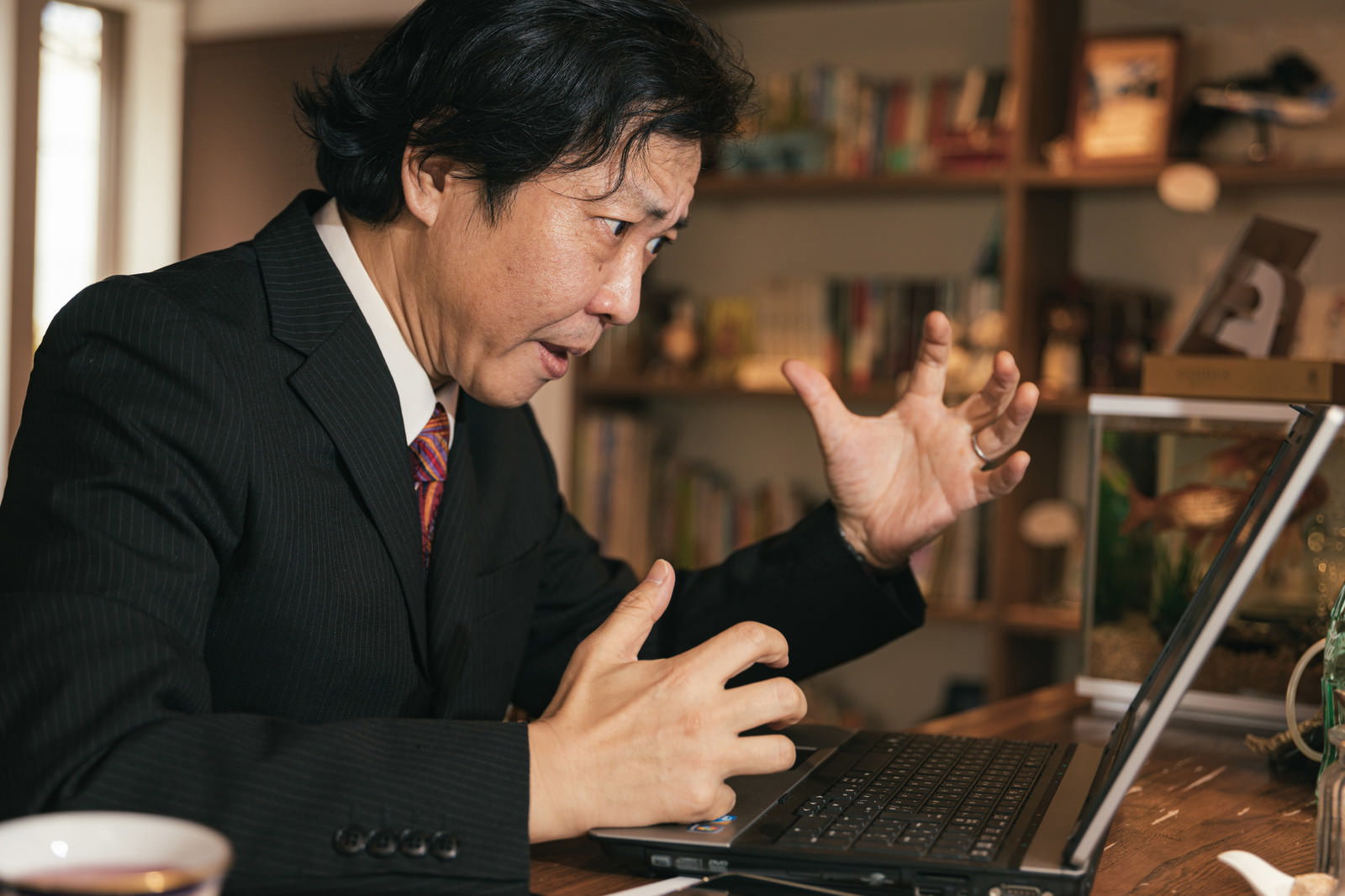 PCの前で怒って声を荒らげる黒いスーツ姿の男性部長［モデル：のせさん］