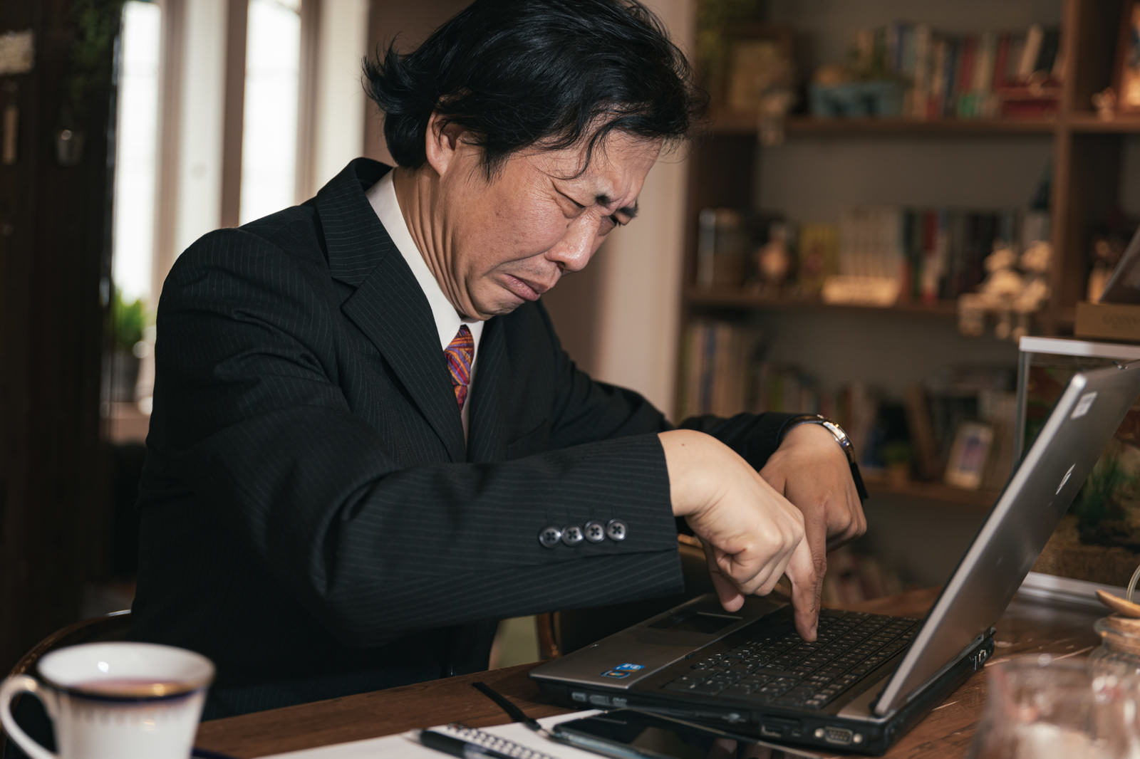 ノートパソコンでタイピングをするスーツ姿の男性［モデル：のせさん］