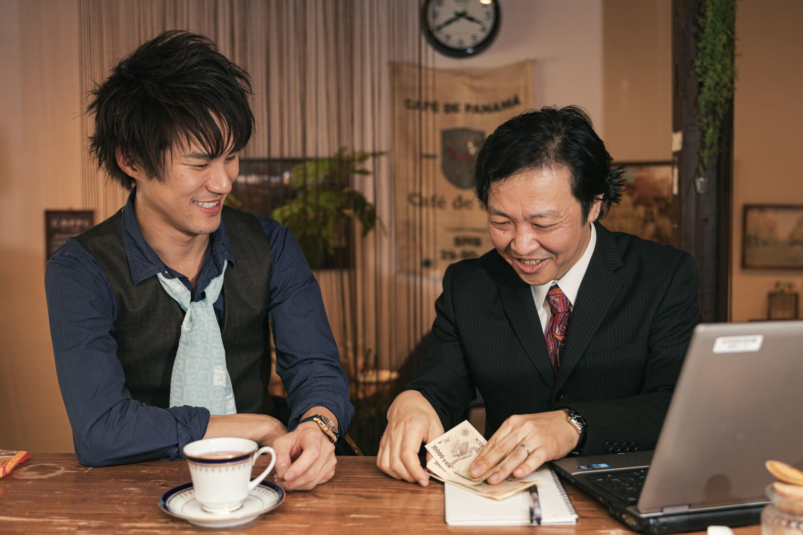 カフェで商談をする男性2人、お金を手にする場面［モデル：のせさん 村田裕章］