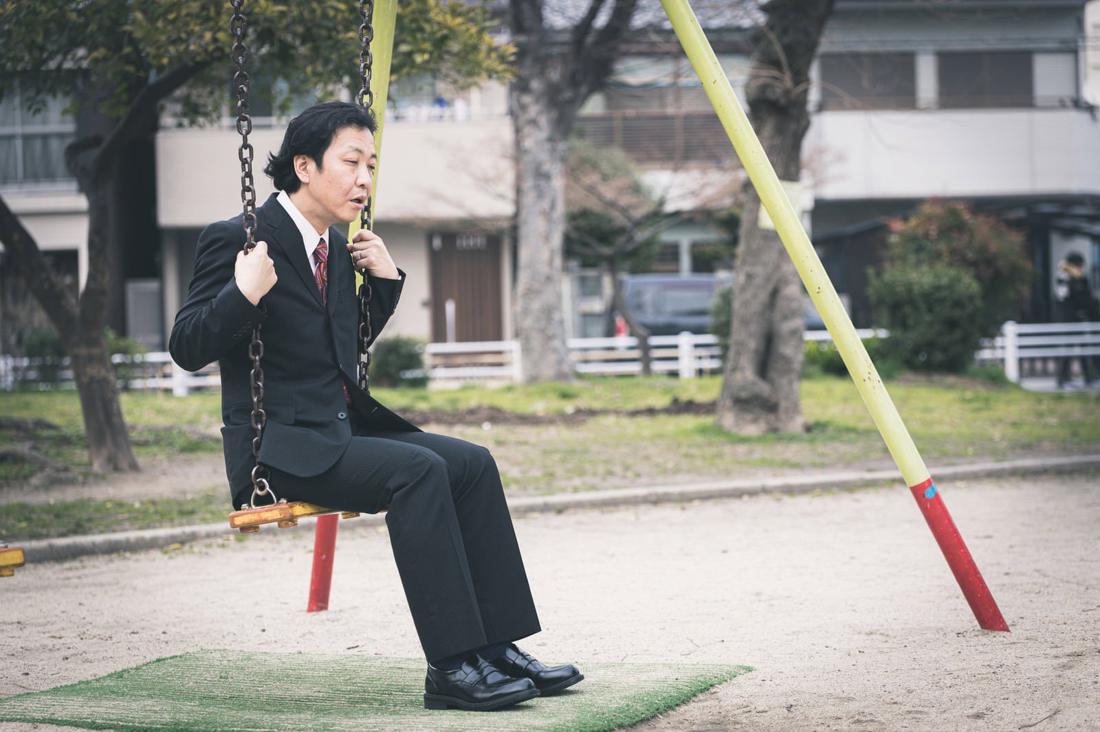 公園のブランコに座るスーツ姿の男性［モデル：のせさん］
