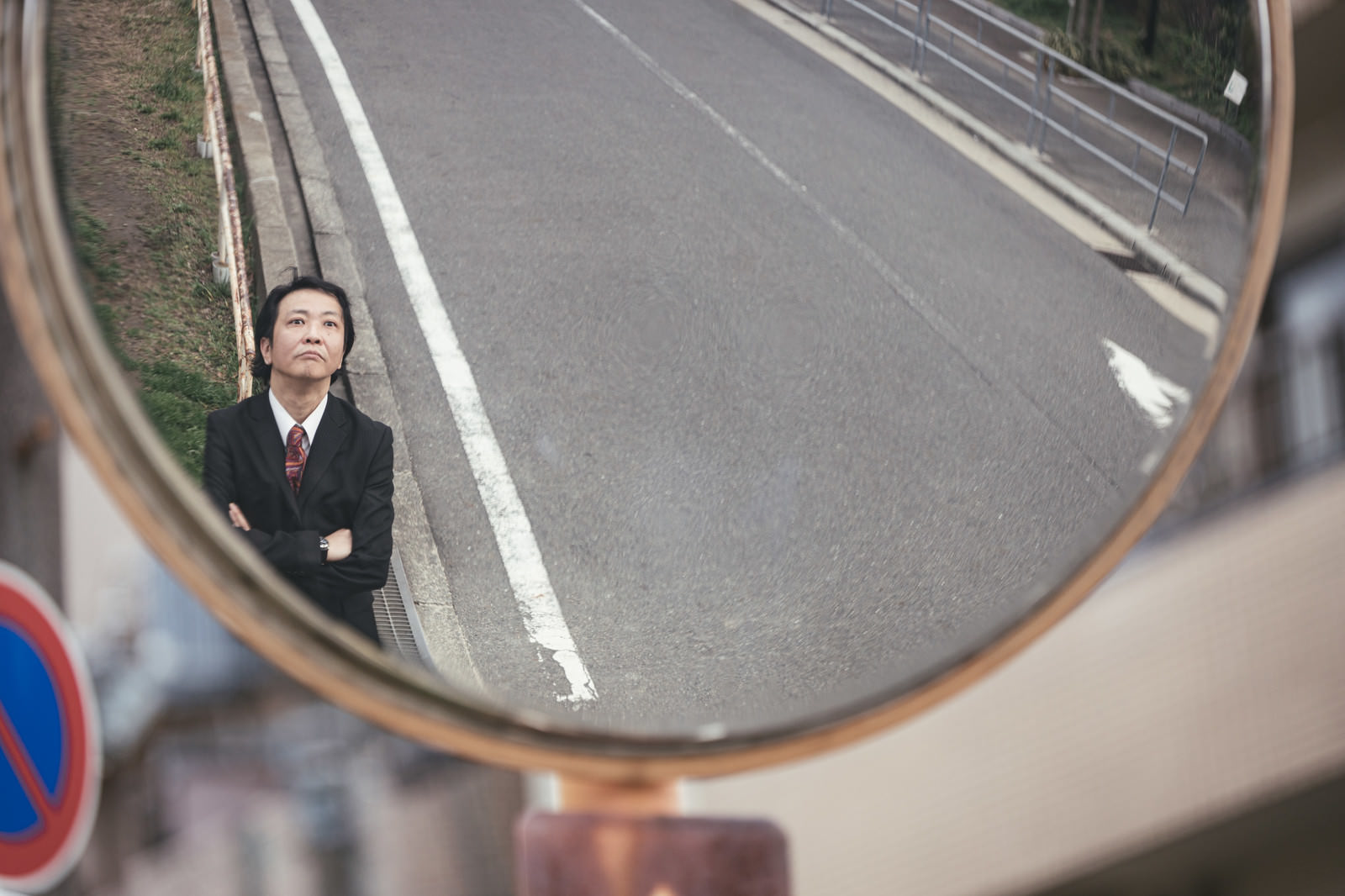 道路のカーブミラーに映る黒いスーツを着た男性［モデル：のせさん］