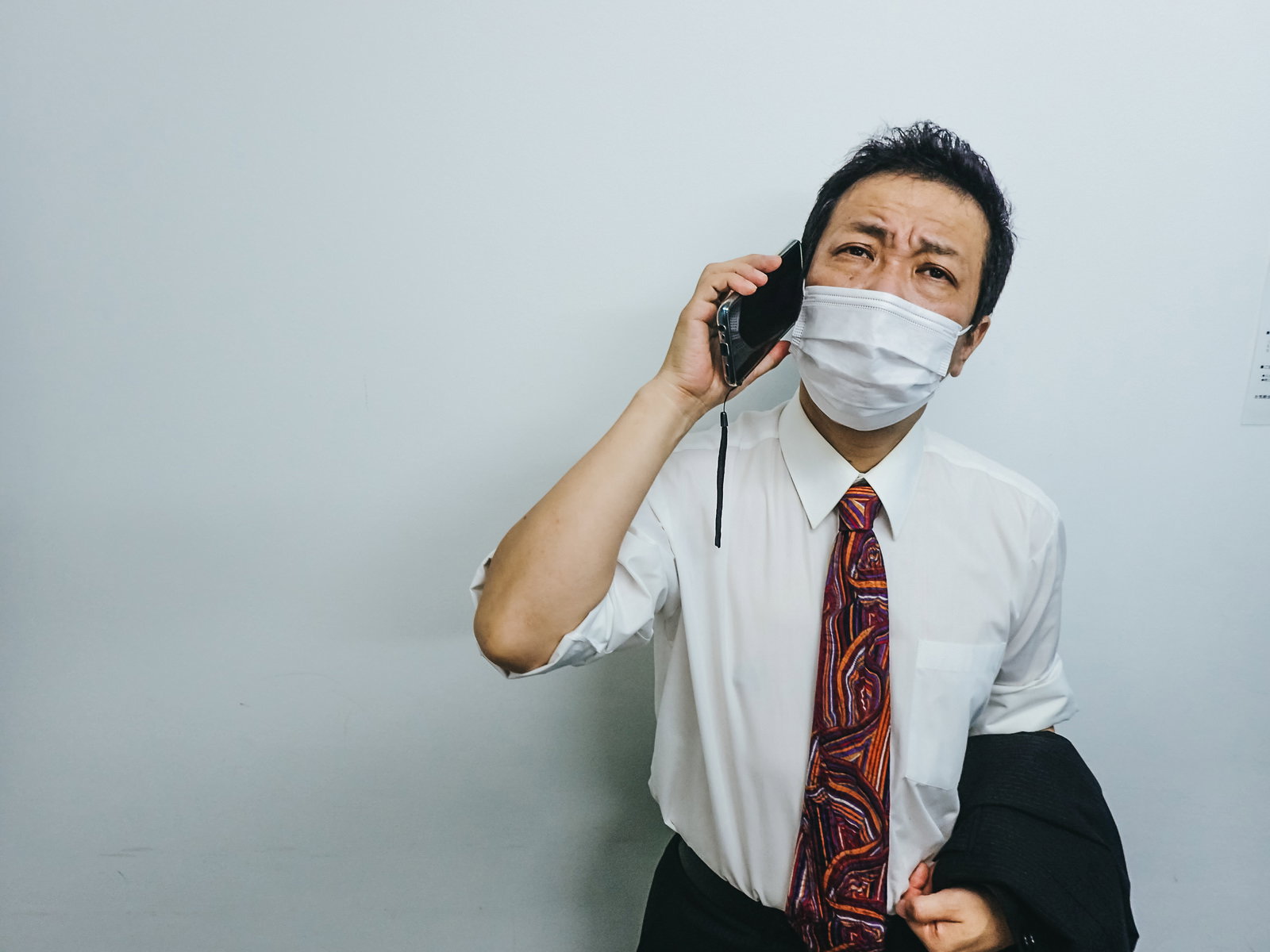 暑さで疲労した表情でマスクをつけた会社員男性が携帯電話で話している［モデル：のせさん］