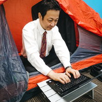 社中泊して残務処理するスーツ姿の男性、キャンプテント内でノートパソコン作業の写真