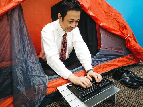 社中泊して残務処理するスーツ姿の男性、キャンプテント内でノートパソコン作業