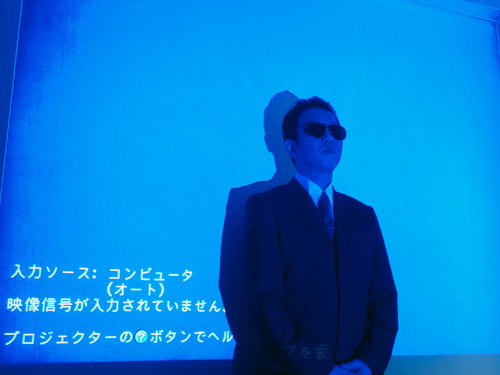 プロジェクターの前で邪魔なんでどいてくれませんかと言うスーツ姿の男性