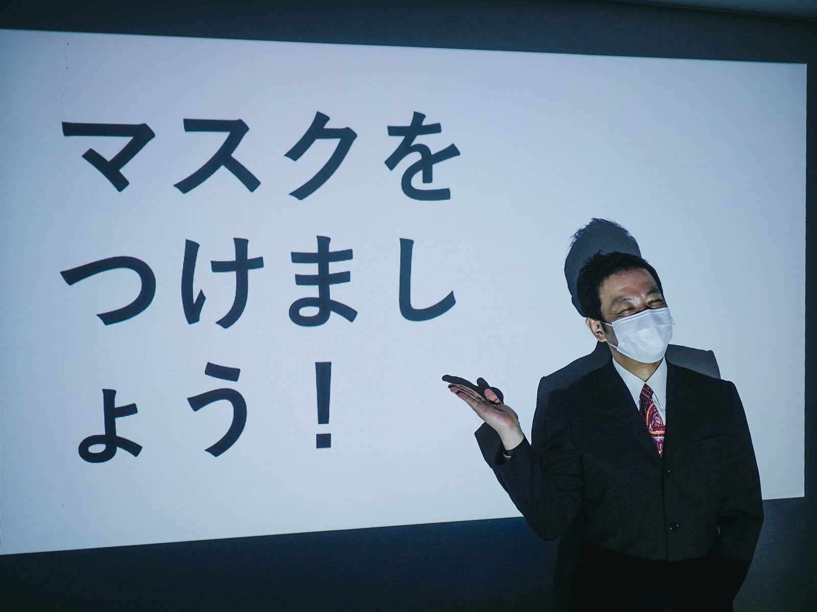 会議室でマスクをつけましょうと呼びかける男性［モデル：のせさん］