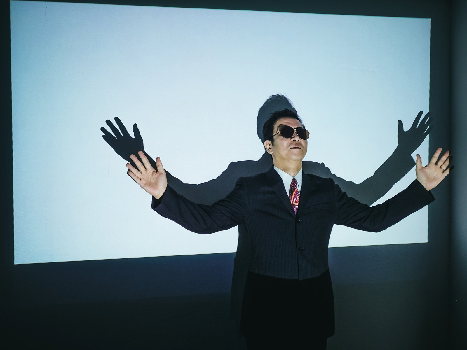 両腕を広げてスクリーン前に立つ男性［モデル：のせさん］
