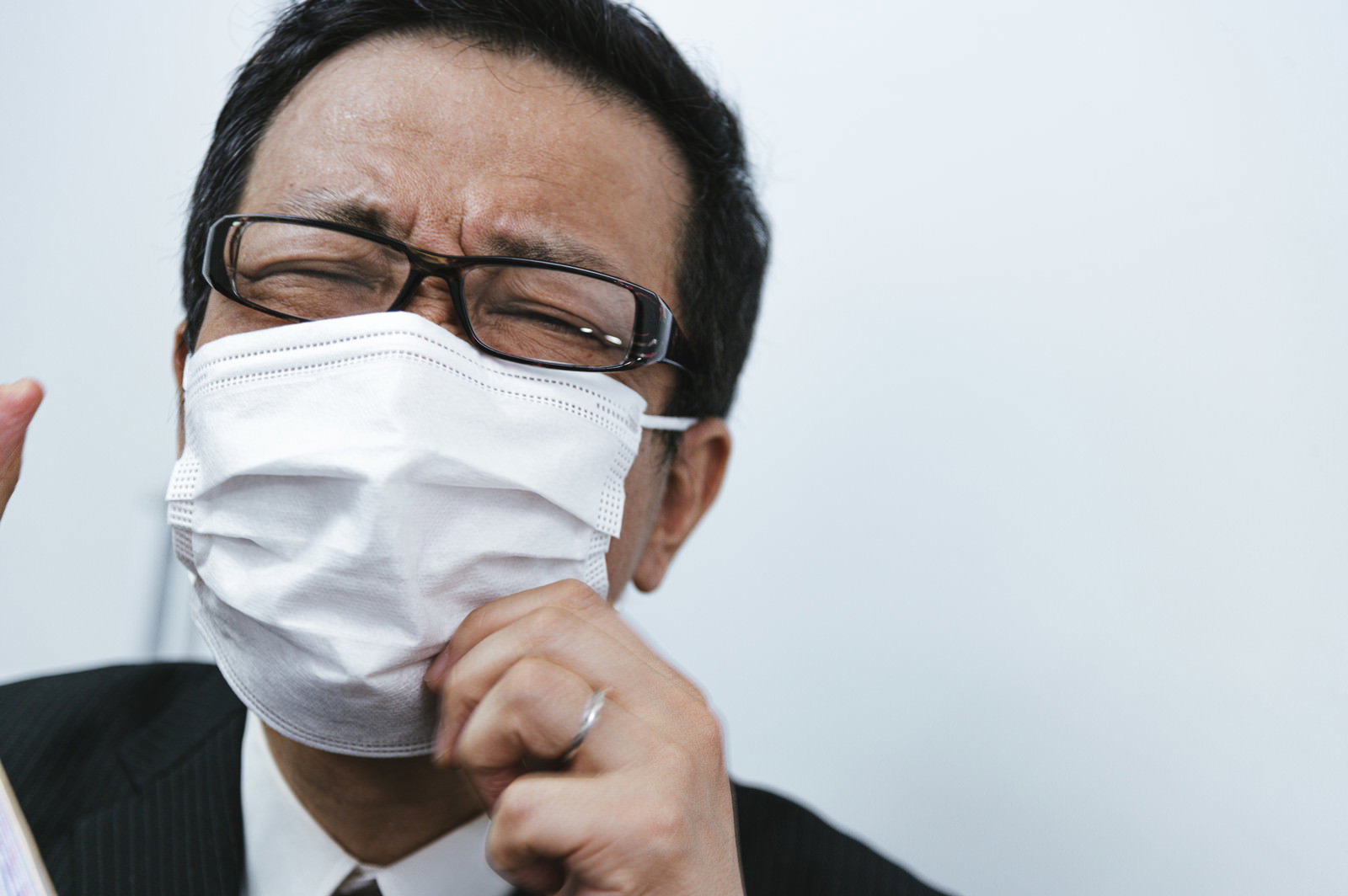 白いマスクを外そうと手をかける眼鏡をかけた男性会社員［モデル：のせさん］