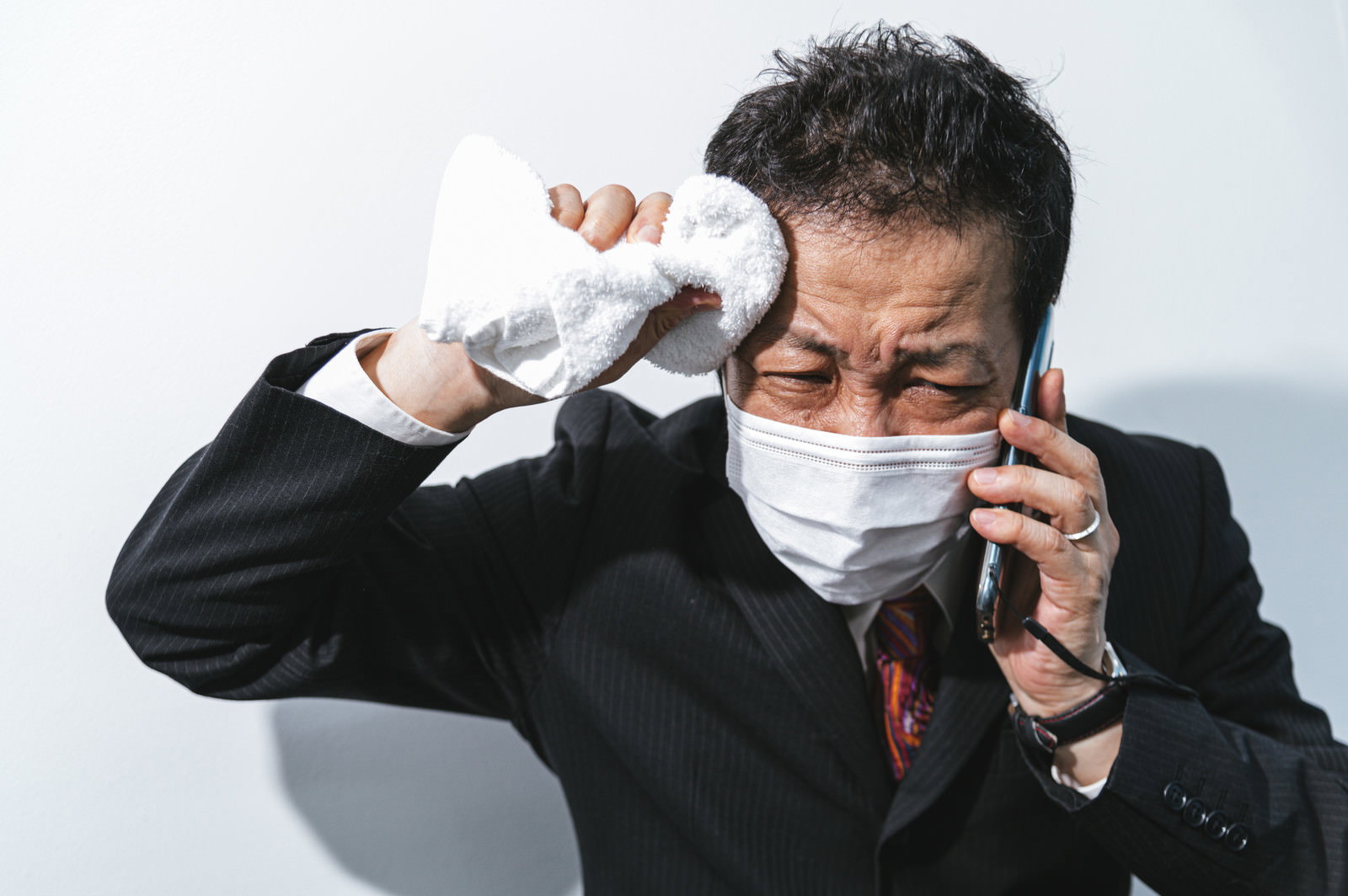 汗をかいてマスクを外そうとするスーツ姿の男性［モデル：のせさん］