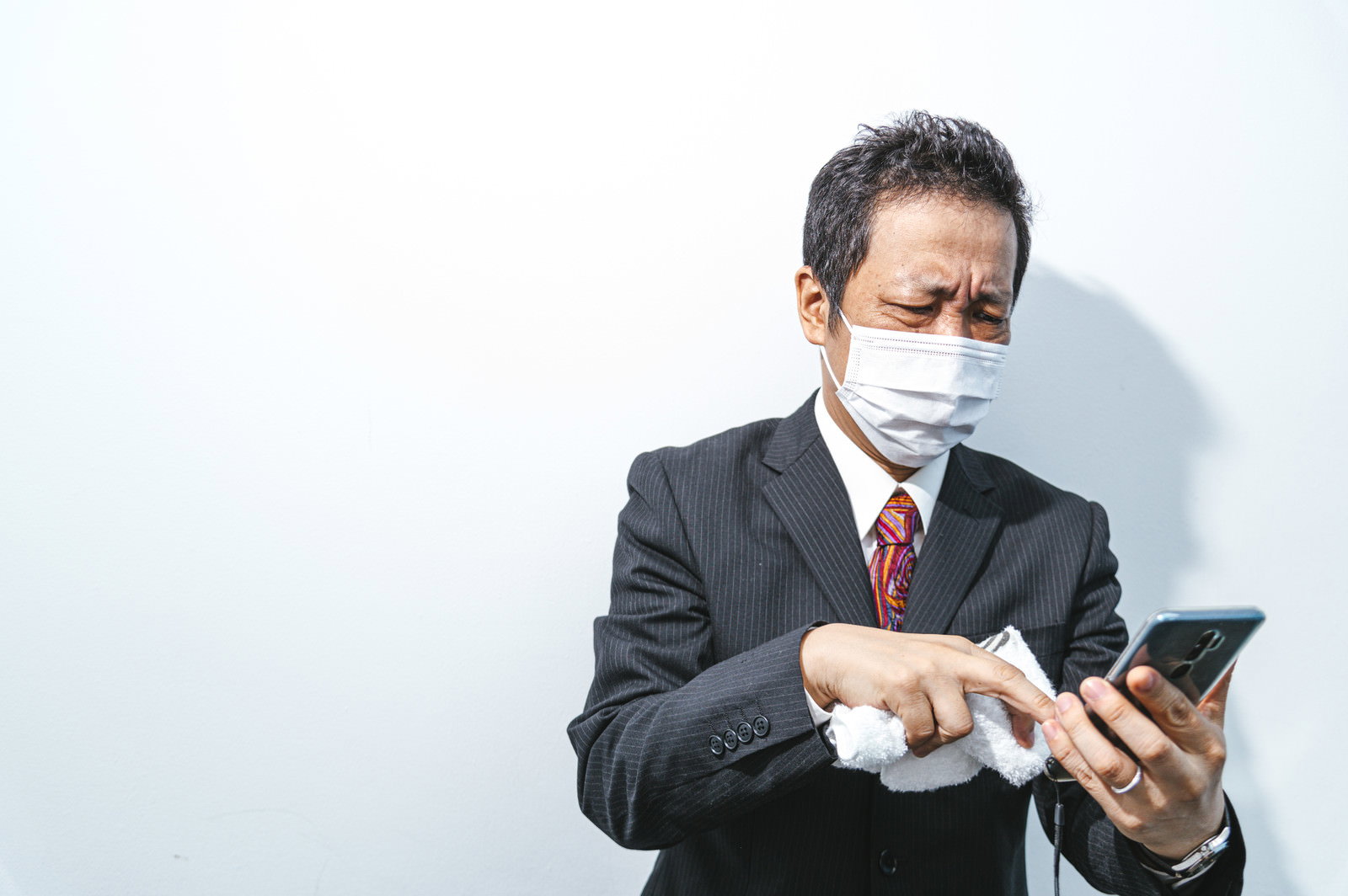 マスクを着用してスマートフォンを見るスーツ姿の男性［モデル：のせさん］