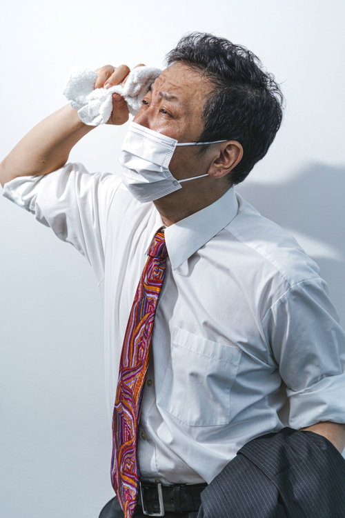 夏日にマスクをして外回りの営業マン、タオルで汗を拭く