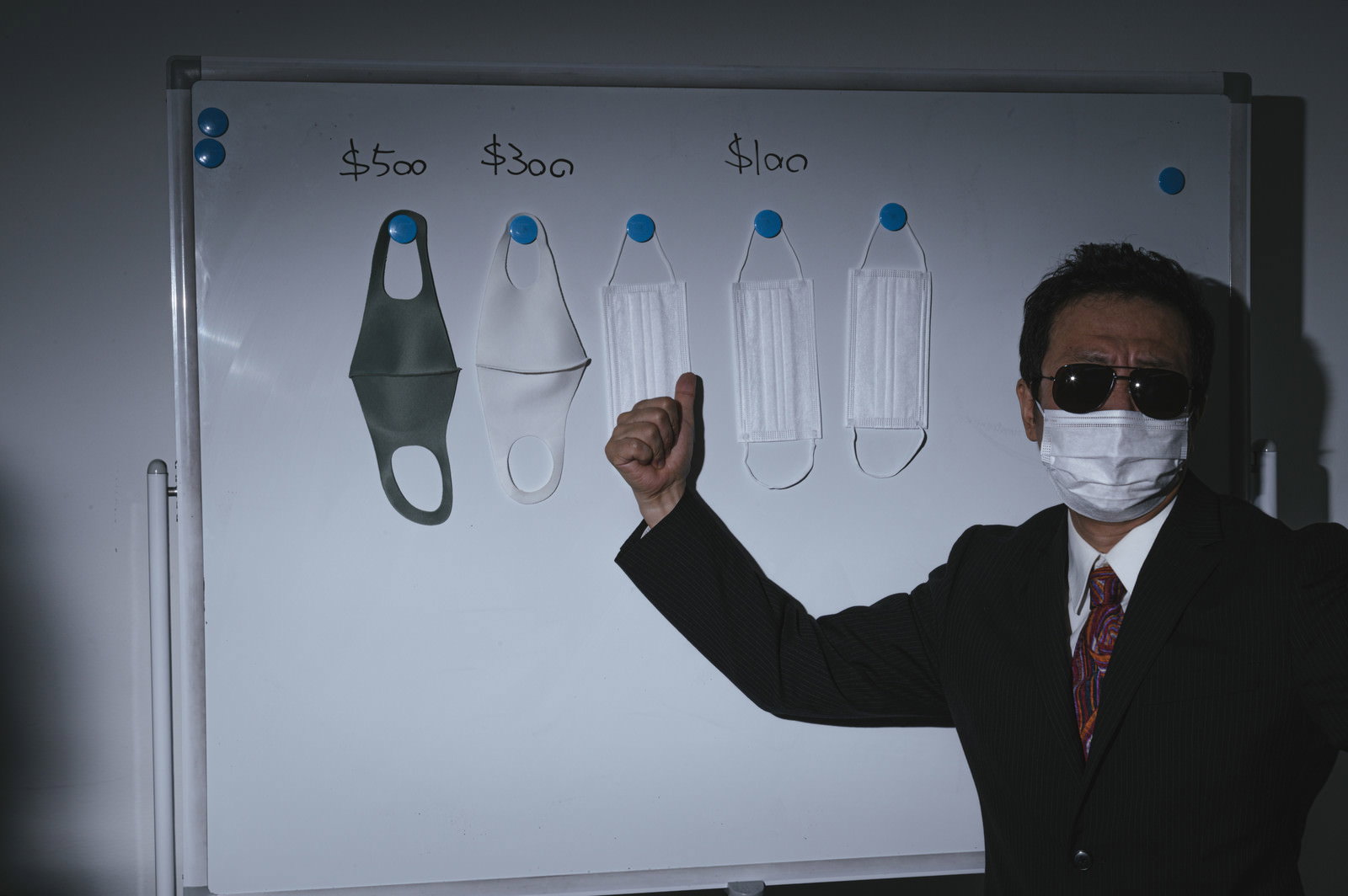 マスクを着用した男性がホワイトボードの前で説明している［モデル：のせさん］