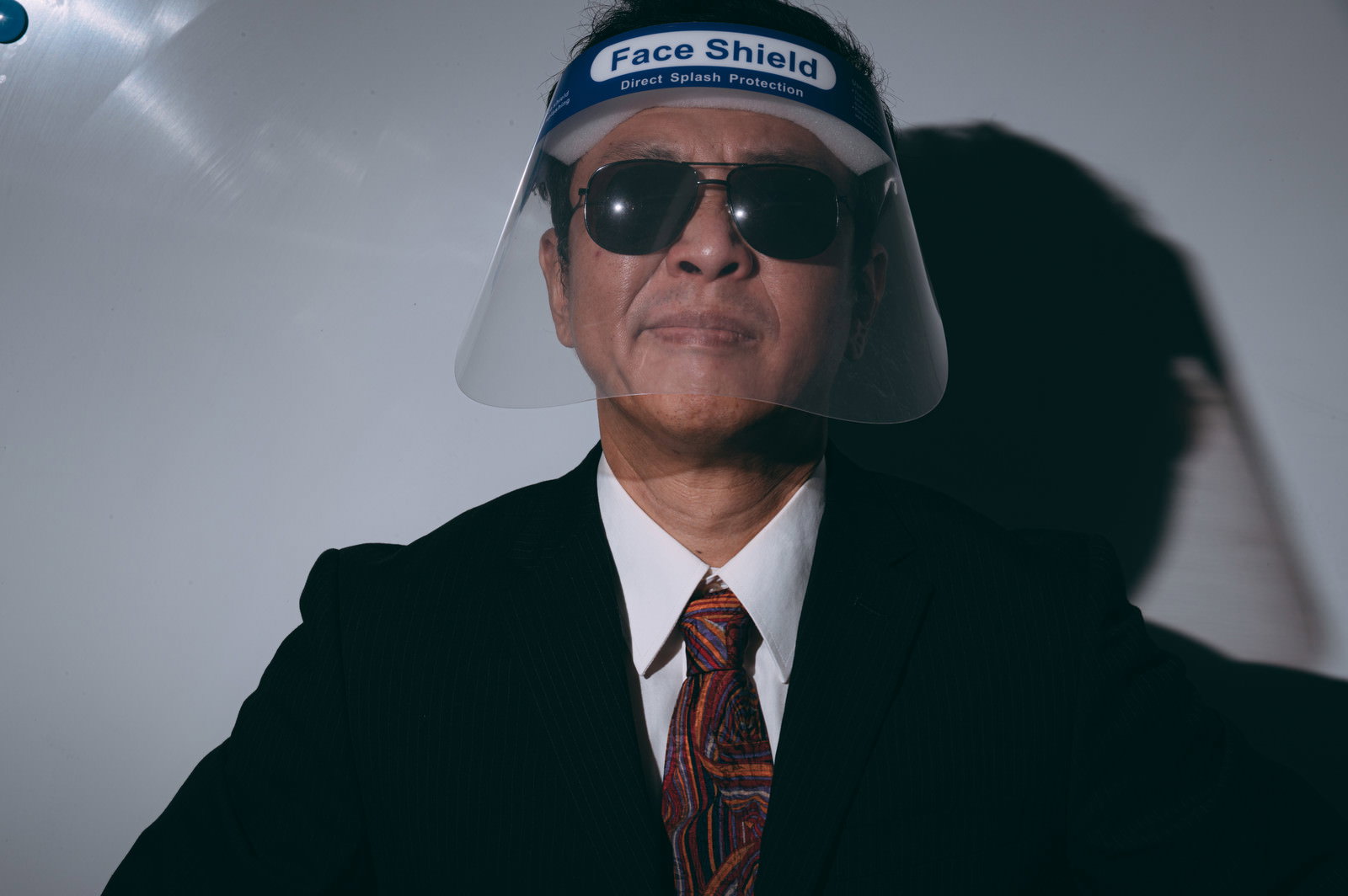 フェイスシールドとサングラスを装着した黒いスーツの男性教官［モデル：のせさん］