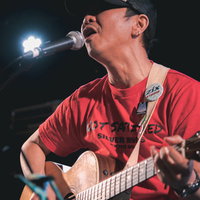 ライブステージで熱唱するアコースティックギターボーカルの男性の写真