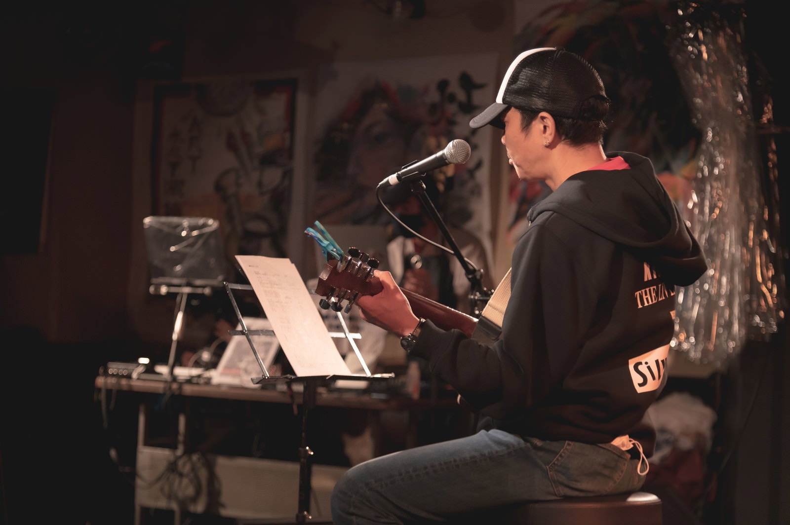 ライブハウスの暗い照明の中でアコースティックギターを弾きながら歌う男性［モデル：のせさん］