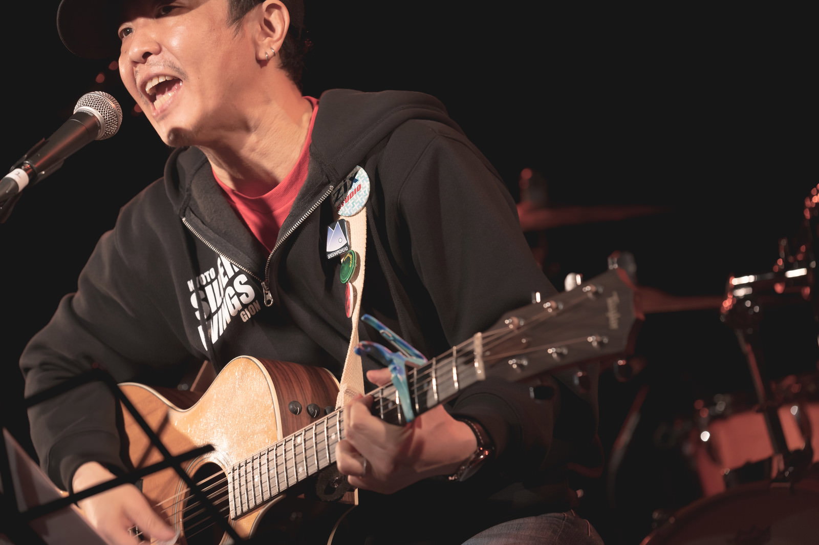 ライブハウスでアコースティックギターを弾きながら歌う男性［モデル：のせさん］