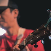 ライブステージで赤いシャツのギタリストが演奏するギターのネックの写真