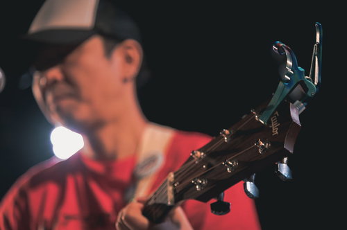 ライブステージで赤いシャツのギタリストが演奏するギターのネック