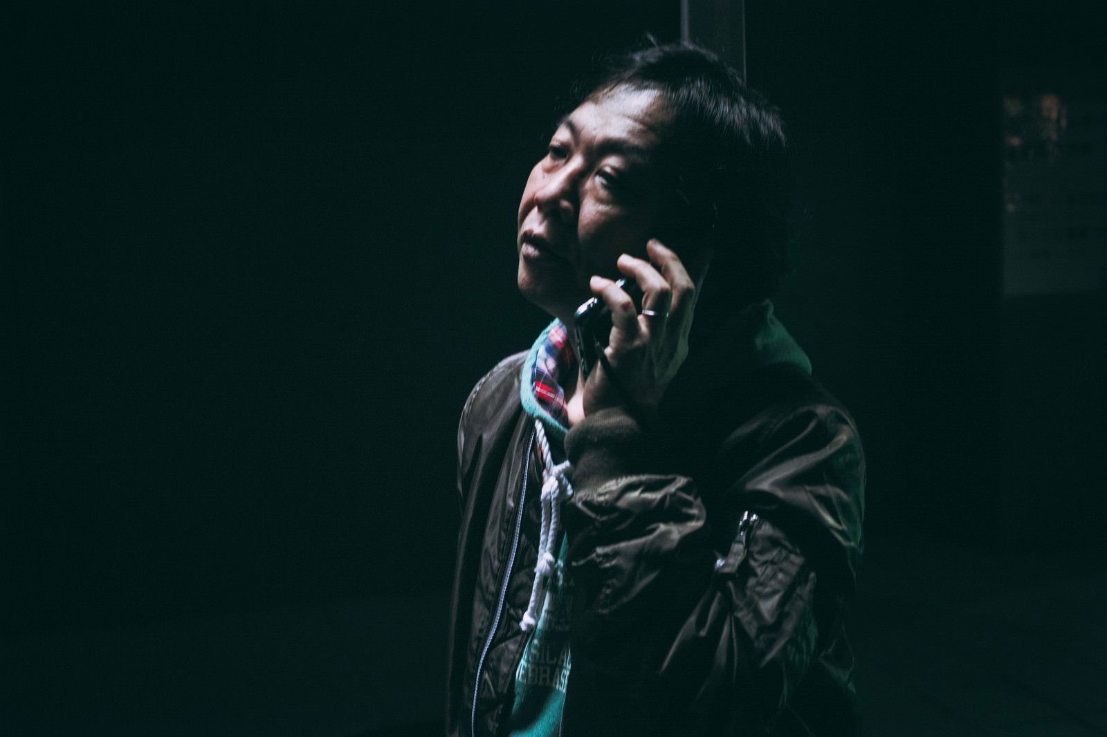 暗い背景でスマートフォンを持ち深刻な表情を見せる中年男性［モデル：のせさん］