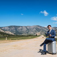 モンゴルの山道でキャリーケースに座ってビジネスをこなすスーツ姿の男性の写真