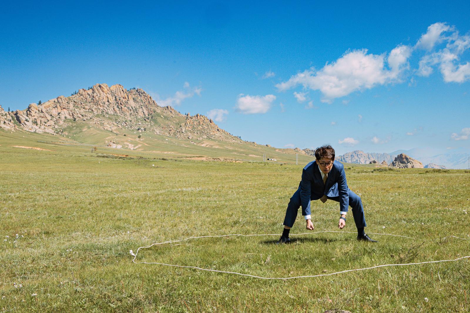 モンゴルの草原でスーツ姿の男性が白いロープの上で四股を踏んでいる［モデル：野崎繁裕］