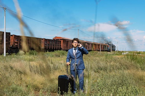 モンゴルの草原で貨物列車を背に通話するビジネスマン