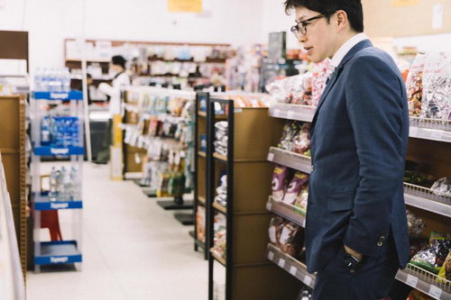 スーパーの売り場で商品を吟味する紺色スーツの男性
