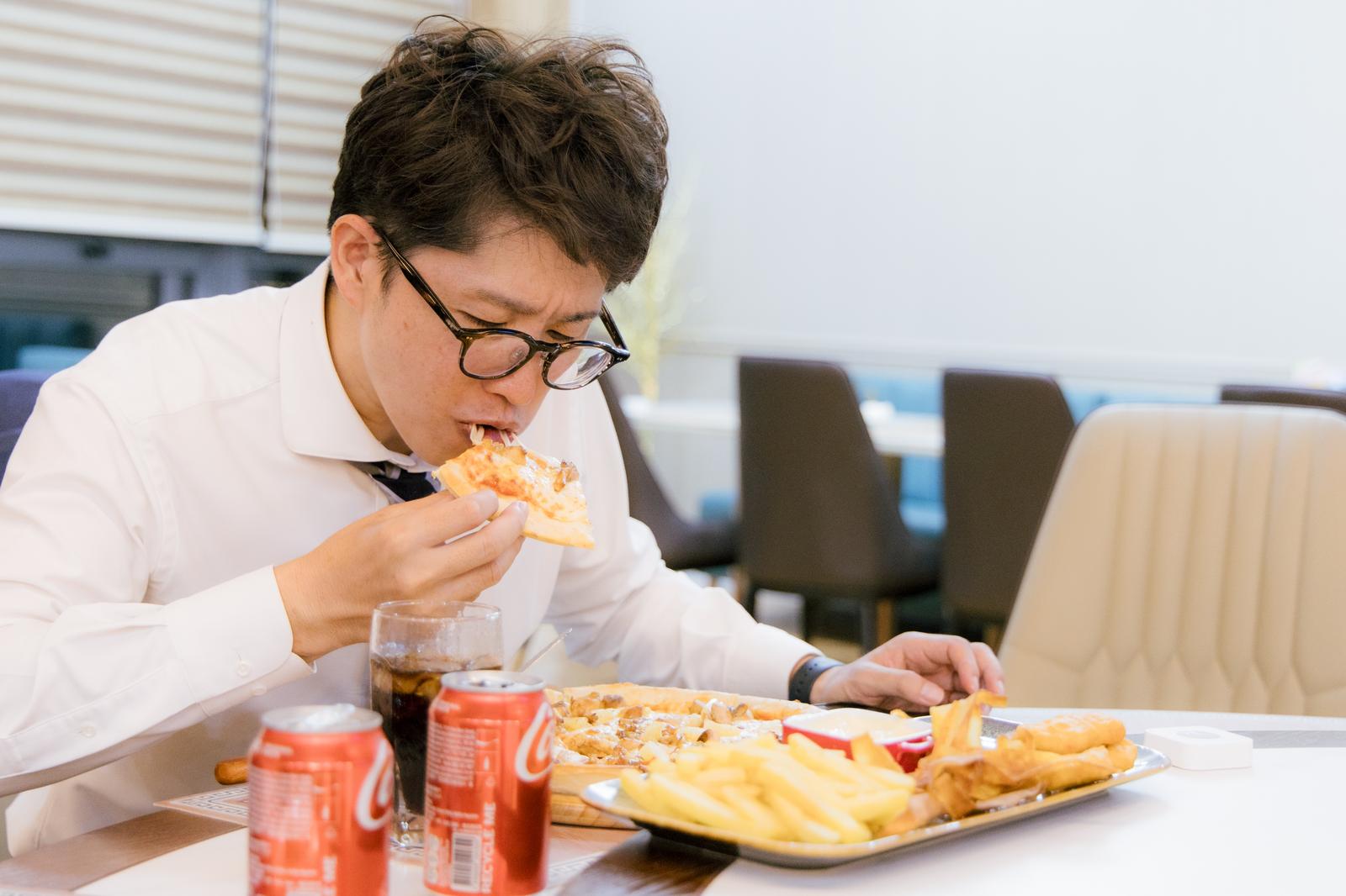白いワイシャツとネクタイ姿の男性がピザとコーラを食べている［モデル：野崎繁裕］