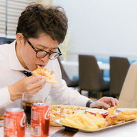 残業後にピザとコーラを爆食いする男性会社員の写真
