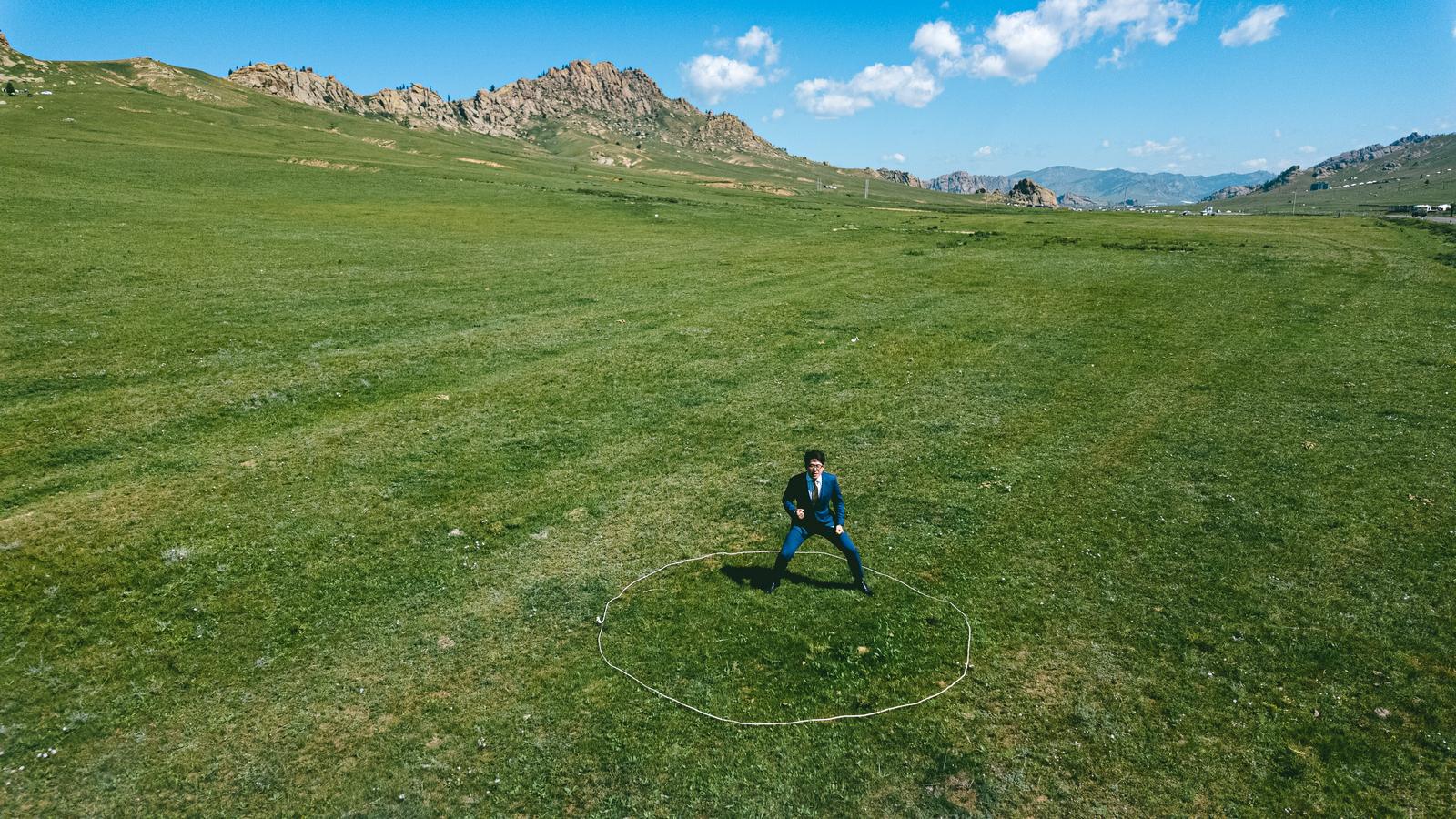 モンゴルの草原で両足を広げて構えるスーツ姿の男性［モデル：野崎繁裕］