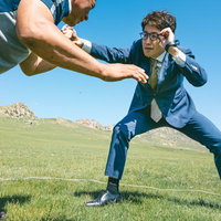 青空の草原で対峙するスーツ姿のビジネスマンと挑戦者の写真