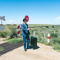 モンゴルの踏切で電車を待つスーツ姿の男性とスーツケースの写真