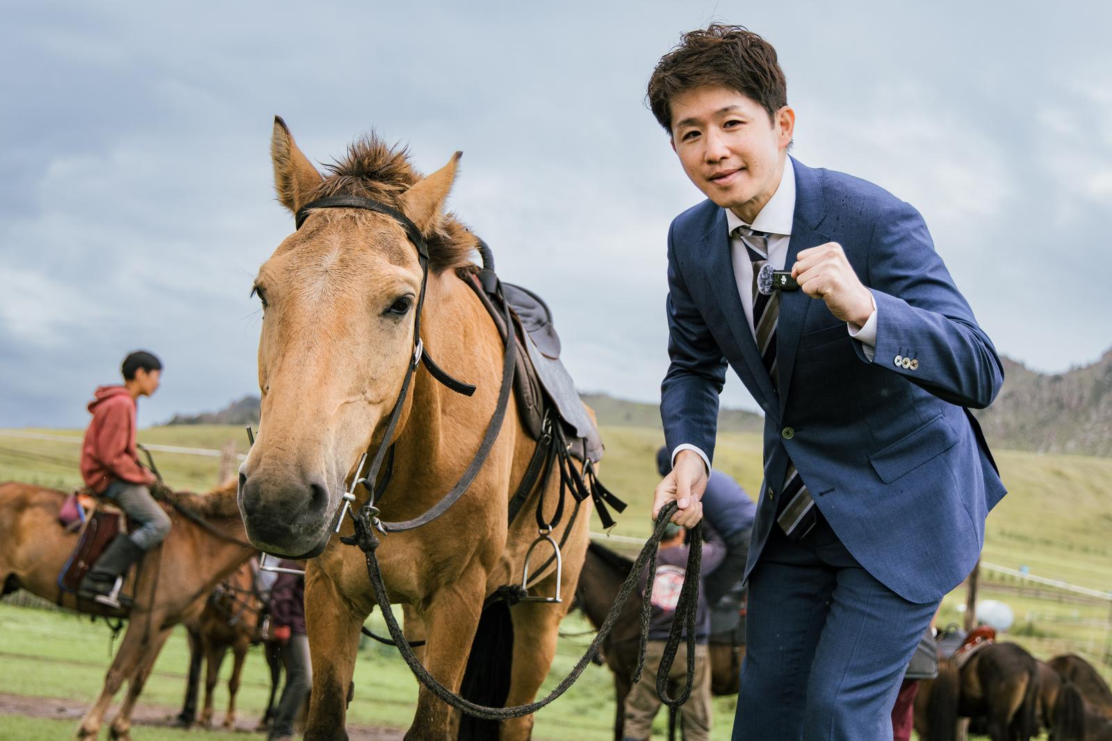 モンゴルの草原で馬の手綱を握るスーツ姿の男性ビジネスマン［モデル：野崎繁裕］