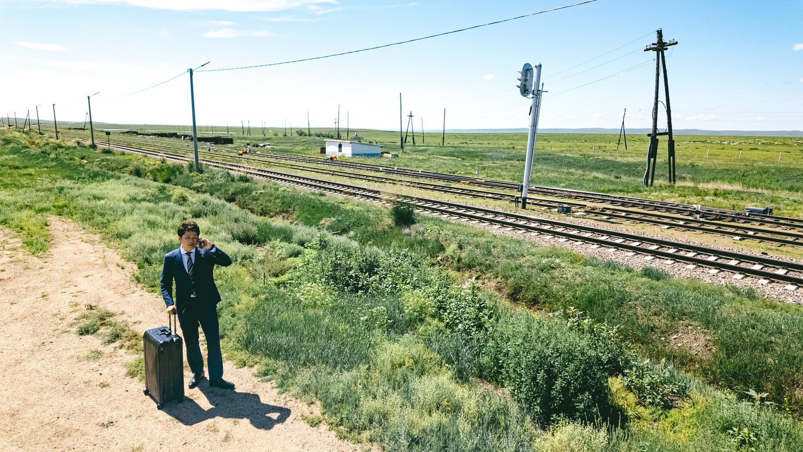 モンゴルの草原で電話をするスーツ姿のビジネスマンと線路［モデル：野崎繁裕］