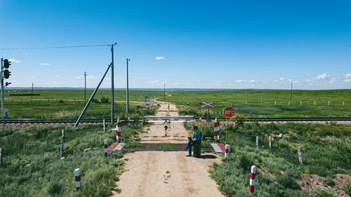 大草原の踏切前でスーツケースに腰を下ろすビジネスマン