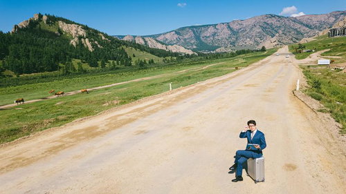 馬が行き交う荒れた道端で仕事をこなすモンゴルのビジネスマン