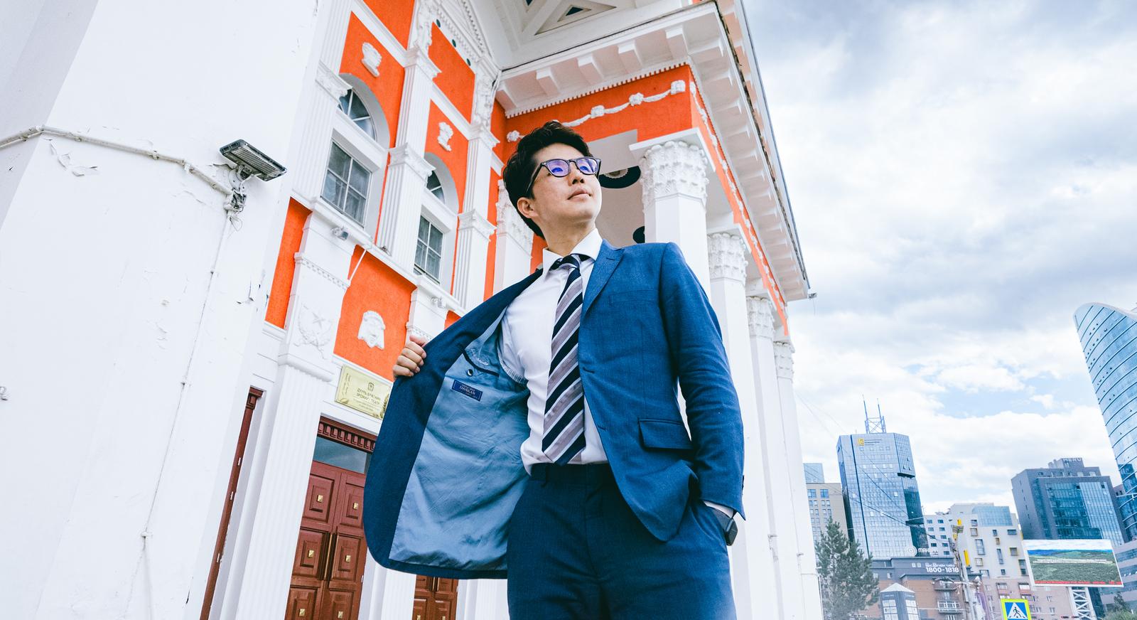 紺色のスーツとネクタイ姿の男性がビル前で上を見上げている［モデル：野崎繁裕］