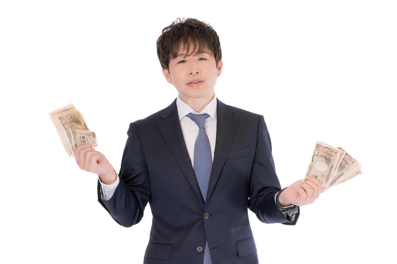 スーツ姿の男性が両手に札束を持って立つ［モデル：野崎繁裕］