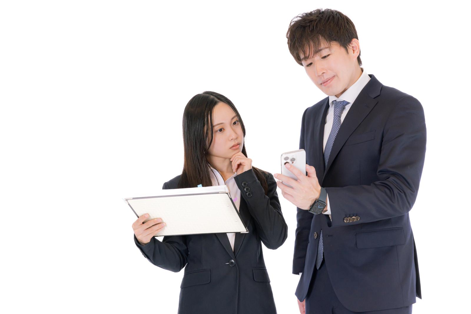 スマートフォンを確認しながら部下に案件を説明するM&Aアドバイザー［モデル：野崎繁裕 吉屋ゆり］