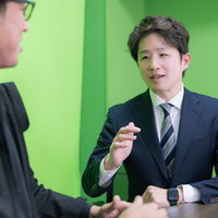 グリーンバックでインタビューを受けるM&Aアドバイザーのスーツ姿の男性の写真