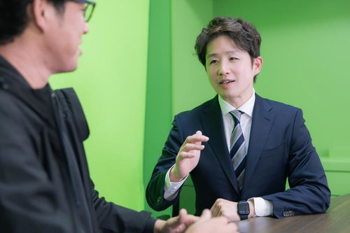 グリーンバックでインタビューを受けるM&Aアドバイザーのスーツ姿の男性