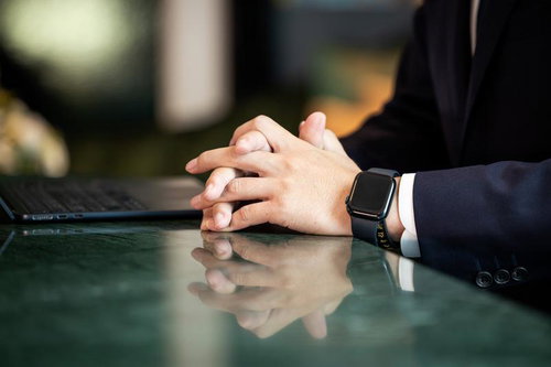 ガラステーブルで手を組み考える紺色スーツの男性