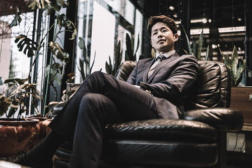 自信に満ちた表情でレザーソファに座るスーツ姿の男性