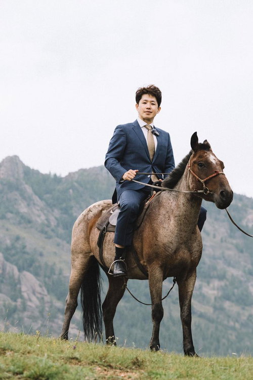 馬上のスーツ姿で颯爽と進むビジネスマン、山道を乗馬で移動