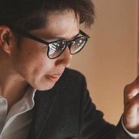 ブラインドの隙間から外を覗く眼鏡をかけた男性の写真