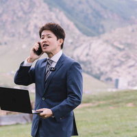 山岳地帯でノートパソコンを持ちながら電話で打ち合わせするビジネスマンの写真