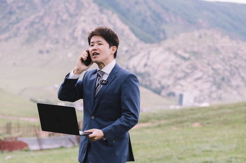 山岳地帯でノートパソコンを持ちながら電話で打ち合わせするビジネスマン